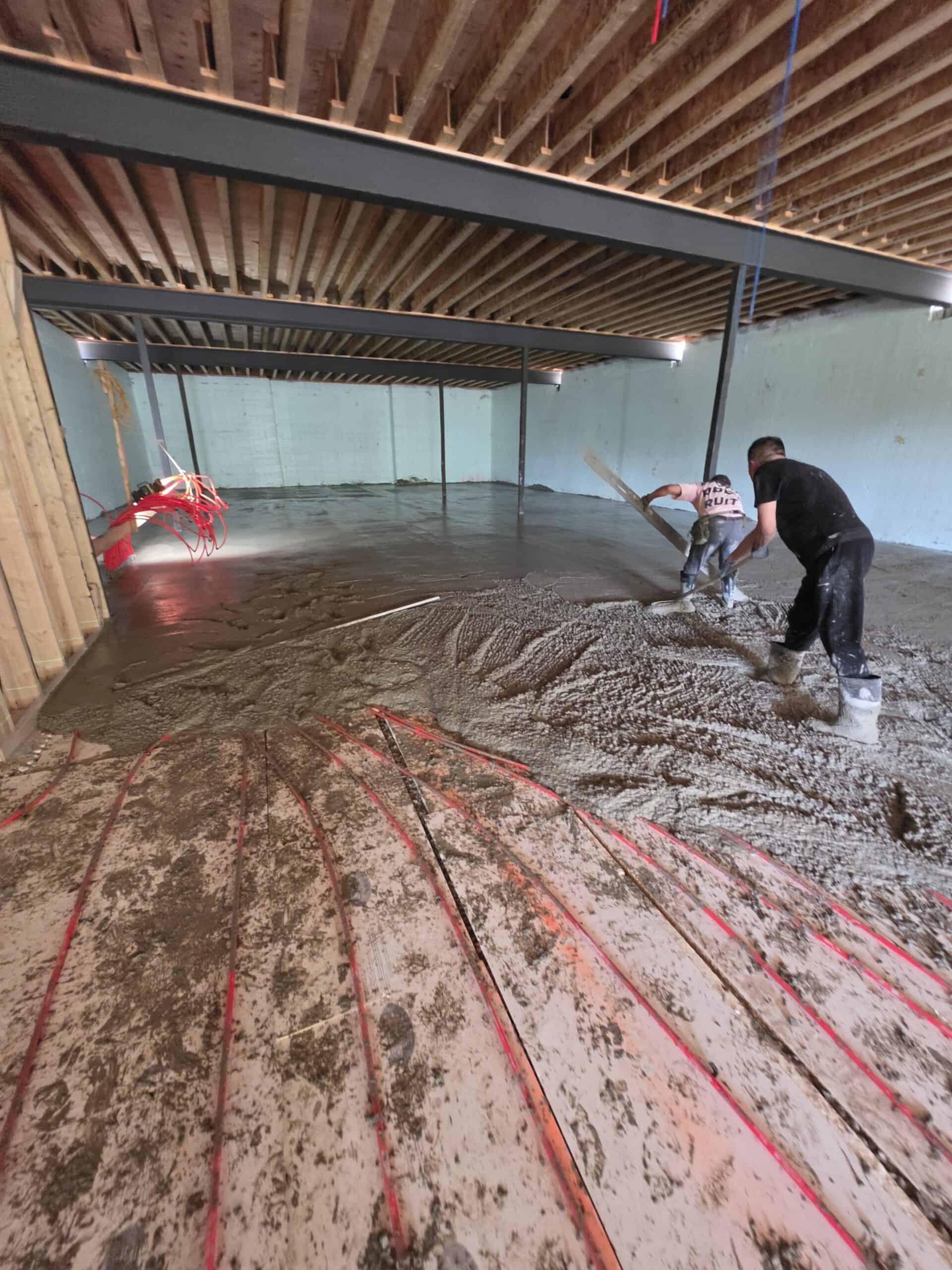 Worker placing concrete indoors for a basement floor using a line pump hose.