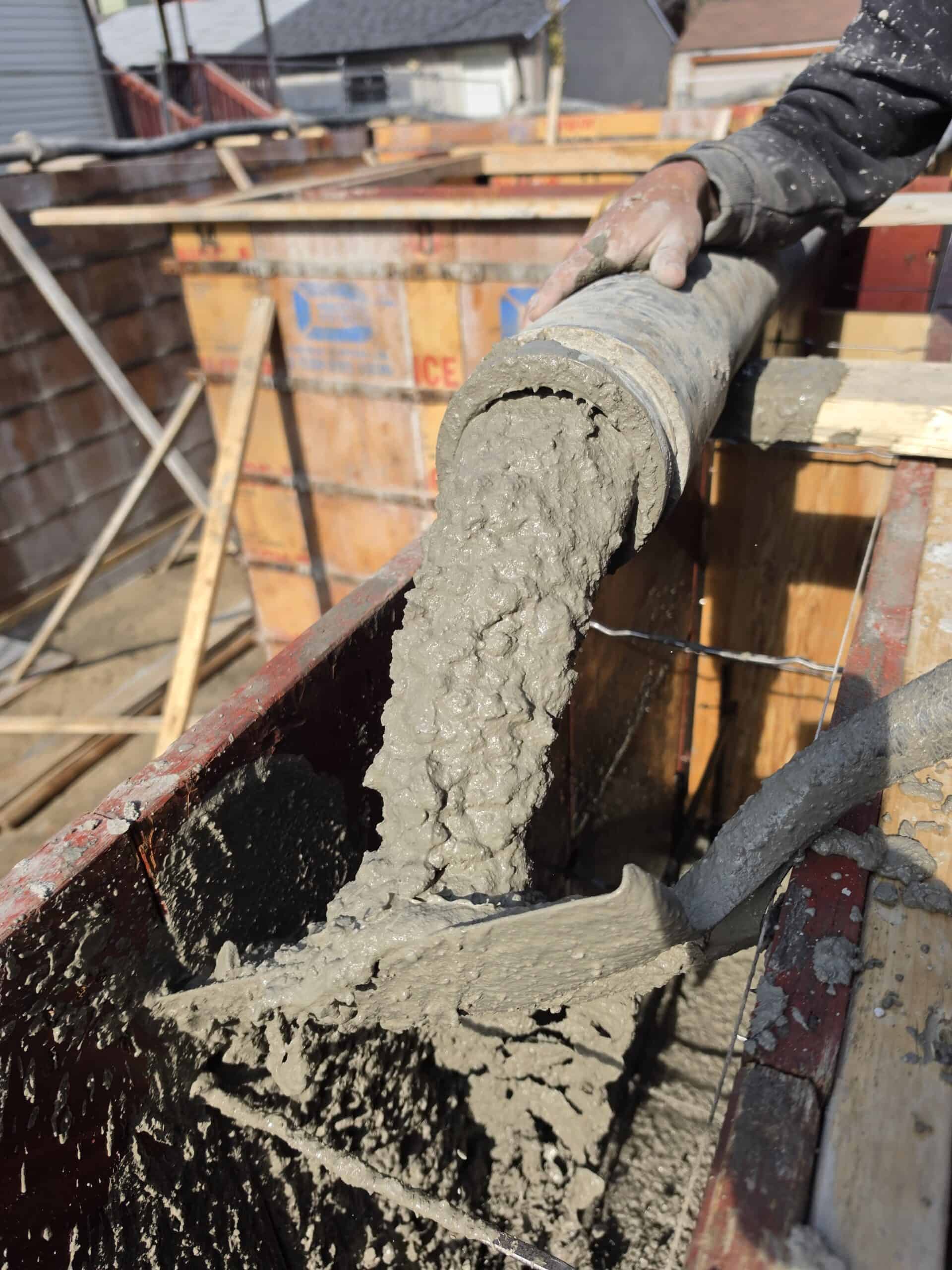Concrete being pumped into foundation formwork through a line pump hose.